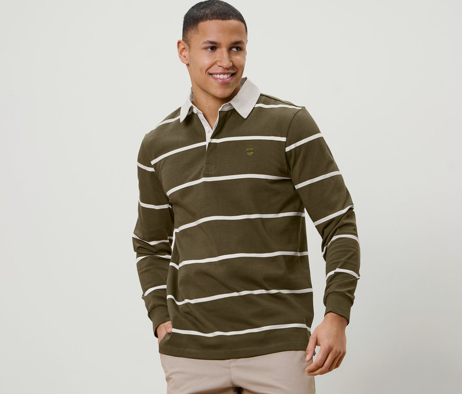 Ein lächelnder Mann mit kurzen Haaren posiert in einem olivgrünen Langarm-Poloshirt mit weißen Streifen.