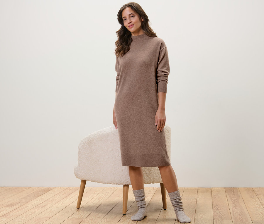 Frau posiert in einem Cashmere-Strickkleid neben einem Teleskop-Schuhanzieher.