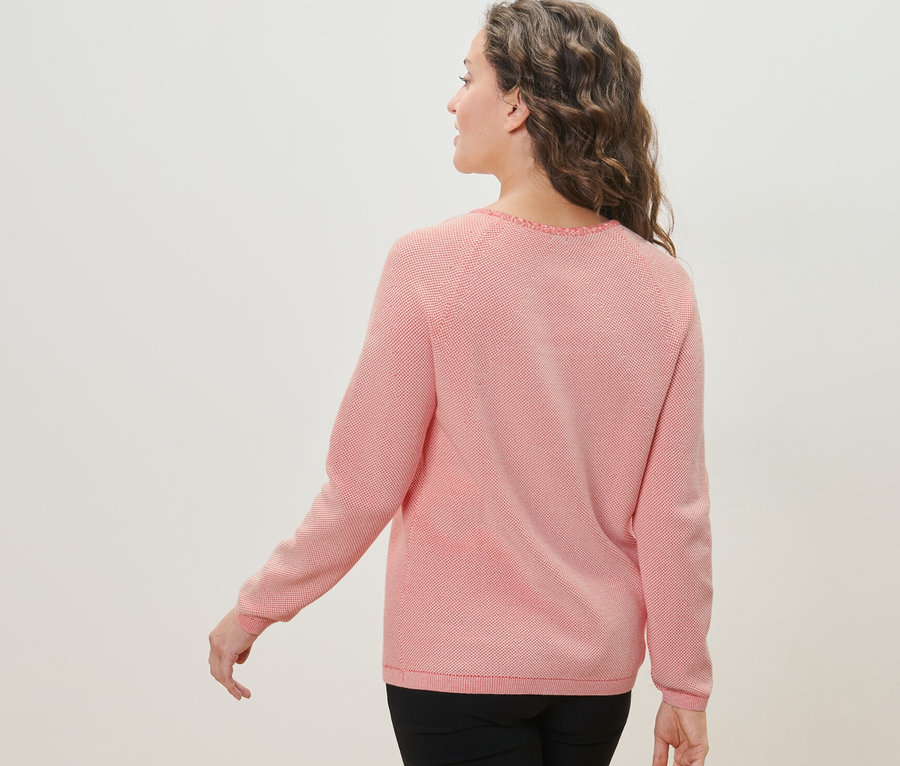 Frau blickt über die Schulter, trägt einen Strickpullover.