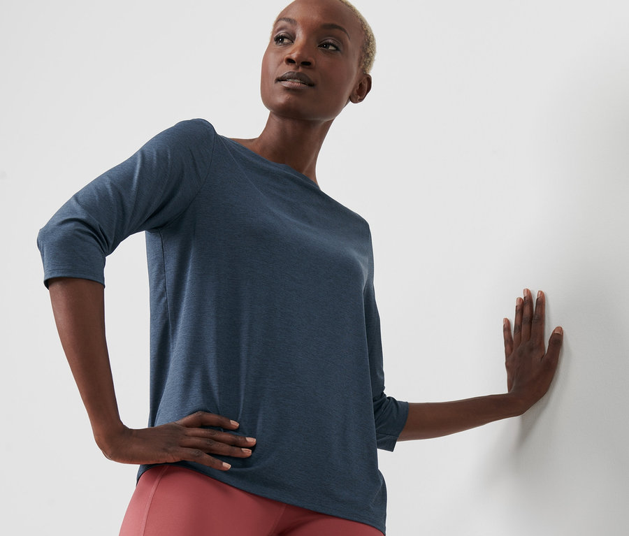 Schwarze Frau posiert in blauem Funktionsshirt mit 3/4-Arm und roten Leggings.
