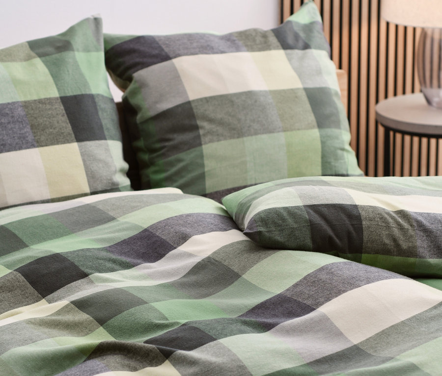 Nahaufnahme von Flanell-Bettwäsche mit grünem, grauem und weißem Karomuster auf einem Bett.