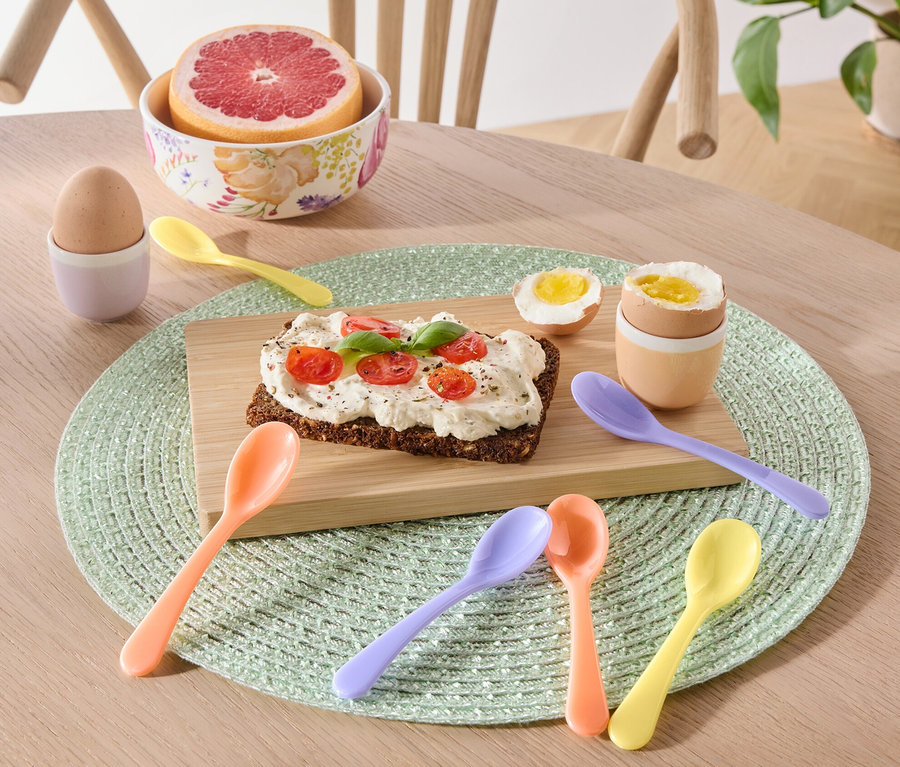 Auf einem Tisch liegen ein Teller mit Toast, ein Ei und eine Grapefruit sowie 6 Eierlöffel.