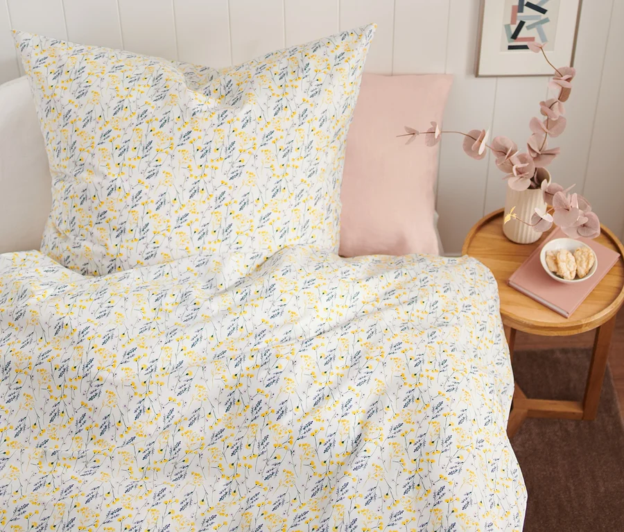 Blumenmuster auf Premium-Baumwoll-Bettwäsche in Normalgröße auf einem Bett. Neben dem Bett steht ein Tisch mit einer Vase und einem Buch.