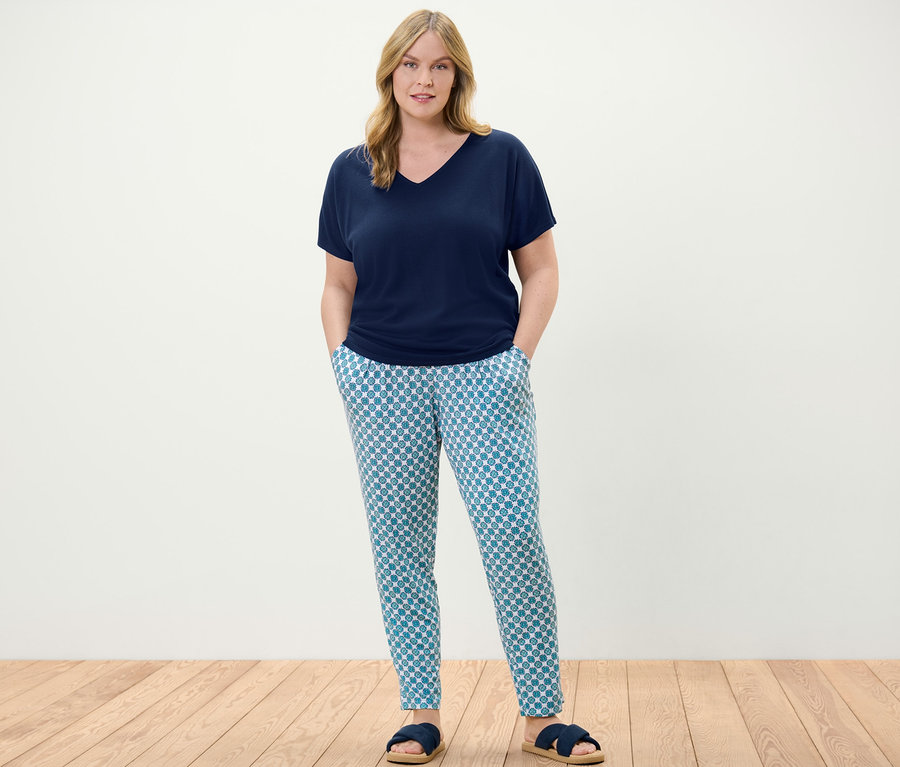 Frau steht und trägt eine dunkelblaue Strukturiertes Shirt und Jerseyhose mit Alloverprint.