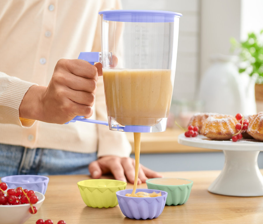 Frau portioniert mit einem Teigportionierer Teig in Silikon-Muffinförmchen.