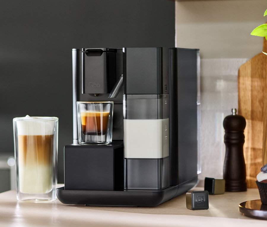 Schwarze Qbo MILK MASTER Velvet Black Kaffeemaschine mit Kaffee und Milch in Gläsern.