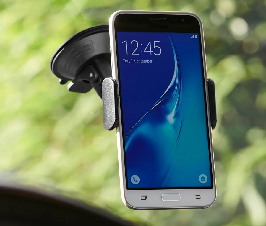 Smartphone in einer schwarzen Halterung an der Windschutzscheibe eines Autos.