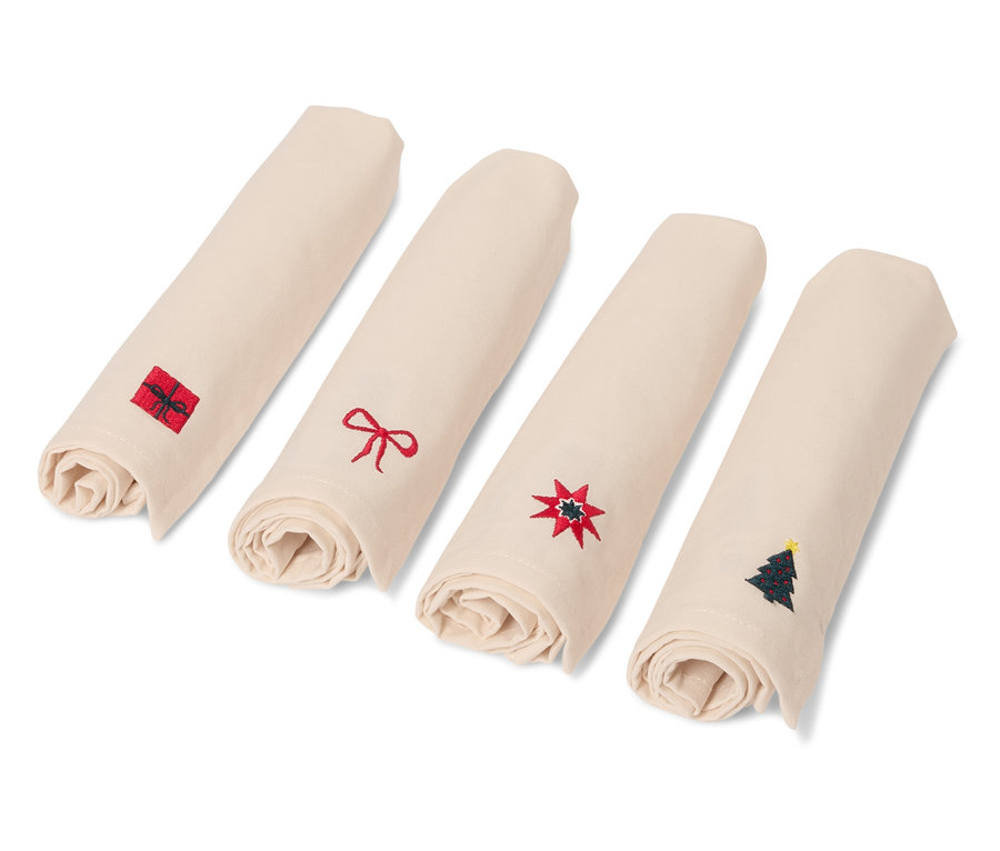Vier zusammengerollte, beige Servietten mit Weihnachtsmotiven.