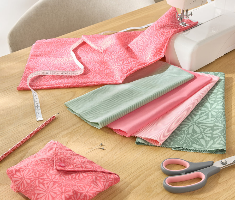 Auf einem Tisch liegen ein 5-teiliges Stoff-Set, eine Nähmaschine, eine Schere, ein Bleistift und ein Maßband.