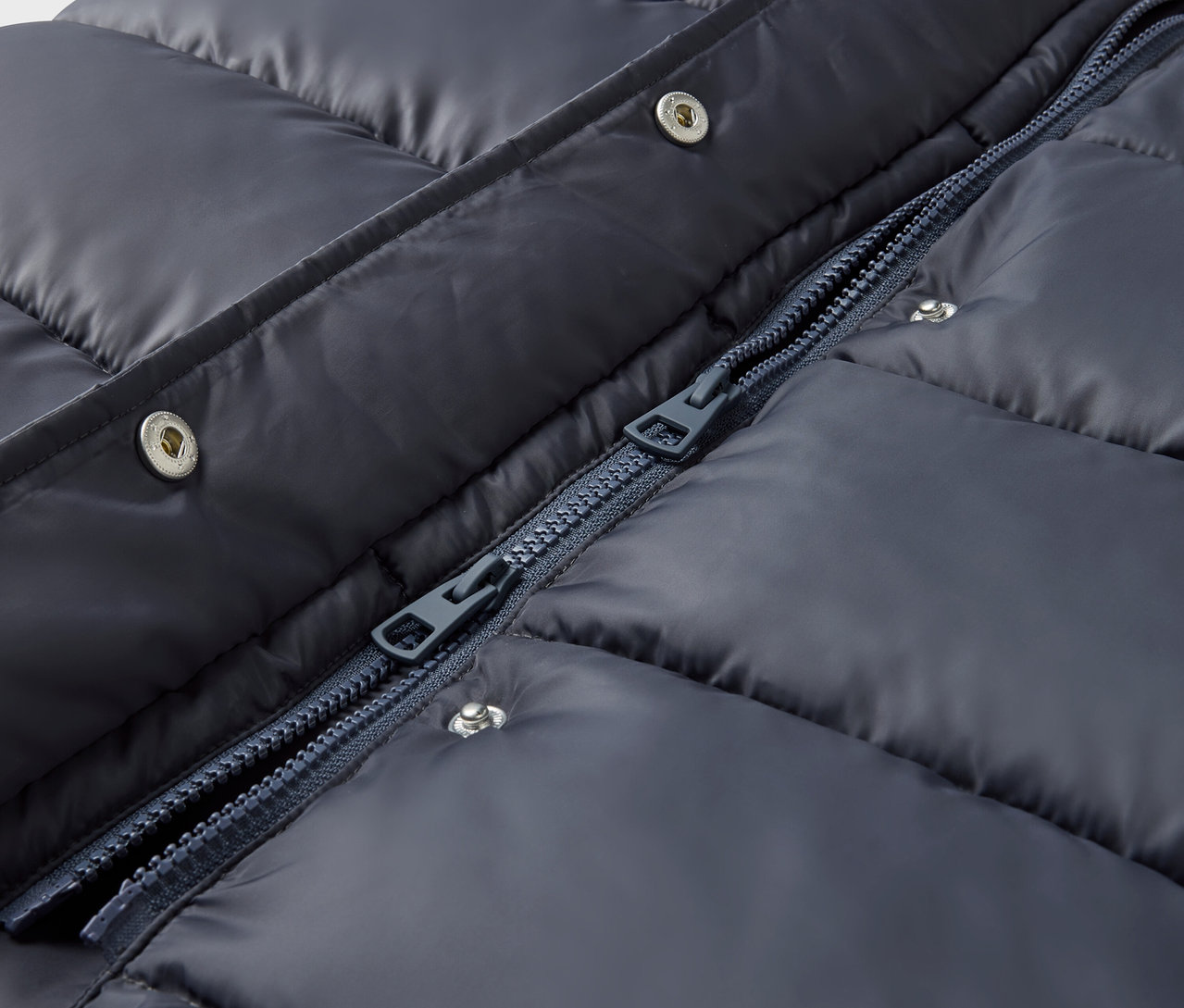 Detailaufnahme einer marineblauen Steppjacke mit silbernen Druckknöpfen und Reißverschluss.