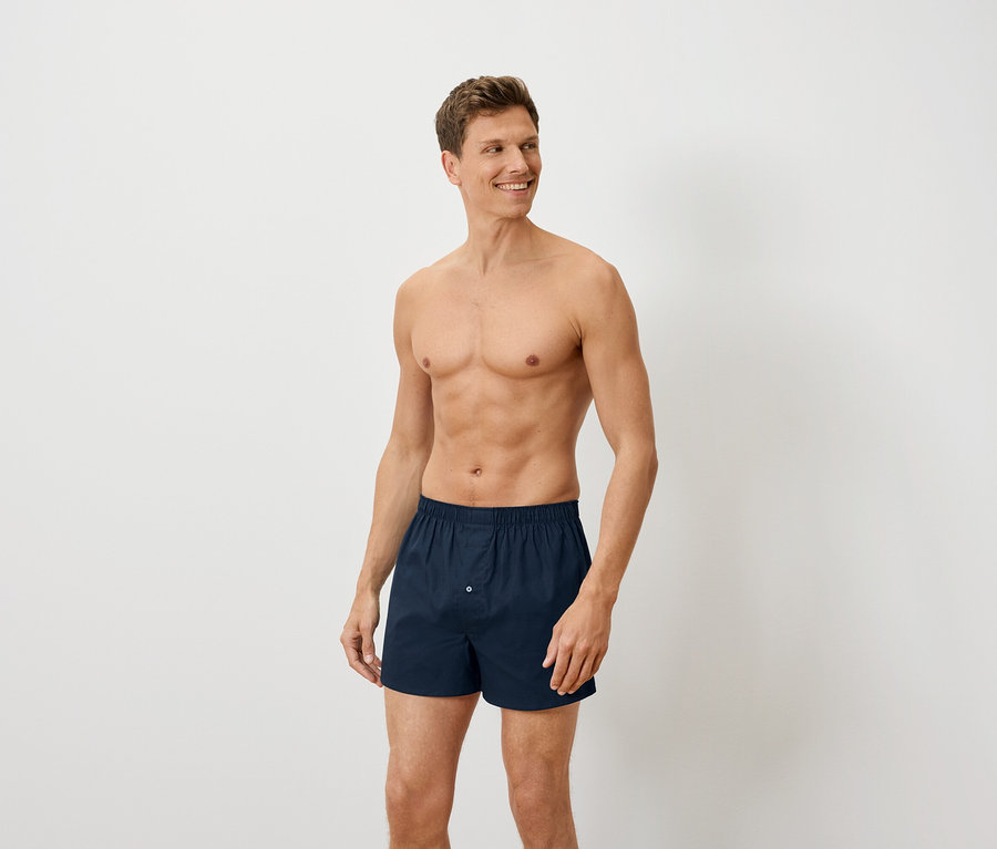 Mann mit freiem Oberkörper posiert in marineblauen Boxershorts.