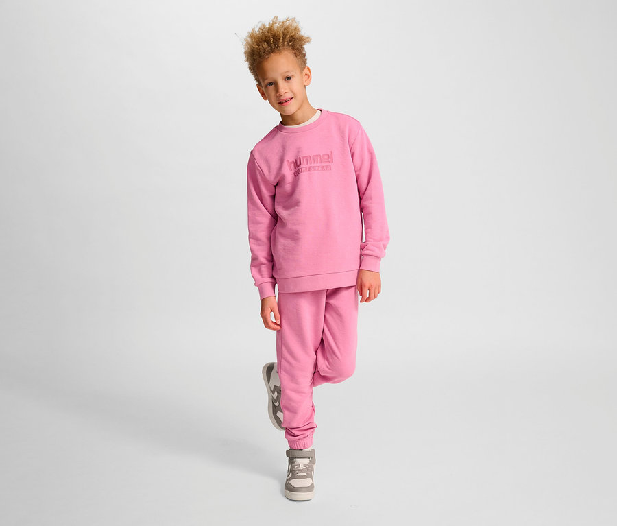 Junge posiert in rosa Hummel HMLJR Base-Sweatshirt und Turnschuhen.