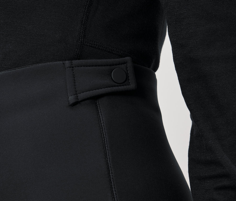 Detailaufnahme einer schwarzen Damenhose mit Knopf am Bund und einem schwarzen Pullover.
