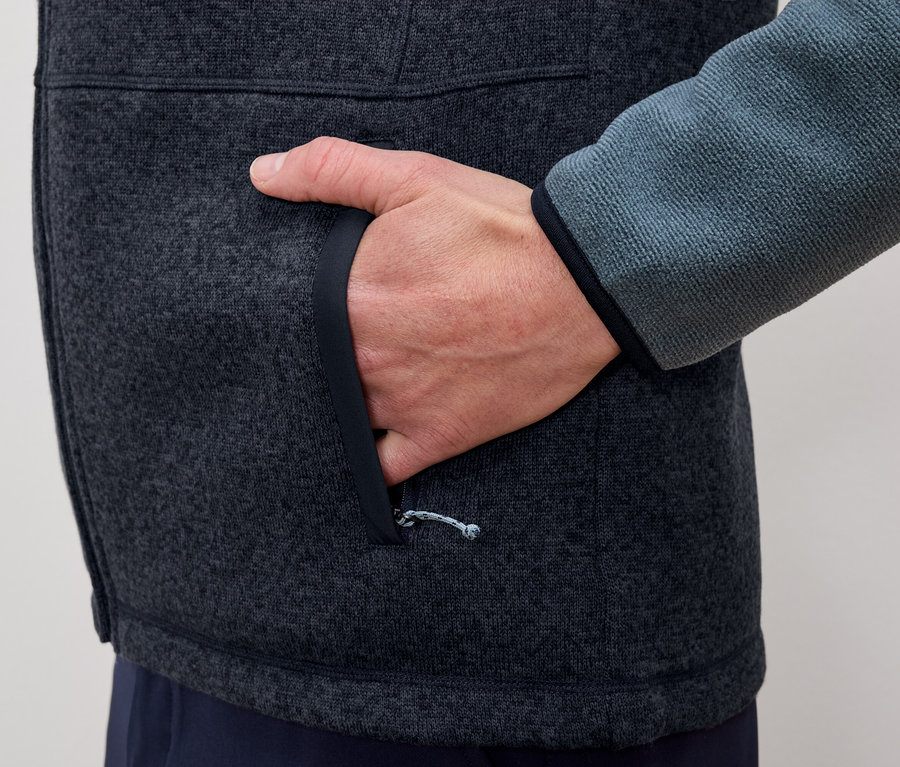 Mann steckt Hand in die Tasche einer grau-blauen Fleecejacke.