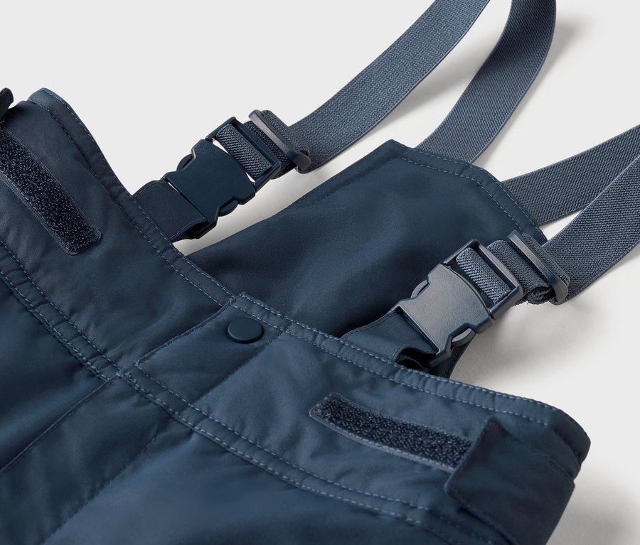 Detailaufnahme einer blauen Latzhose mit grauen Trägern und Kunststoffschnallen.