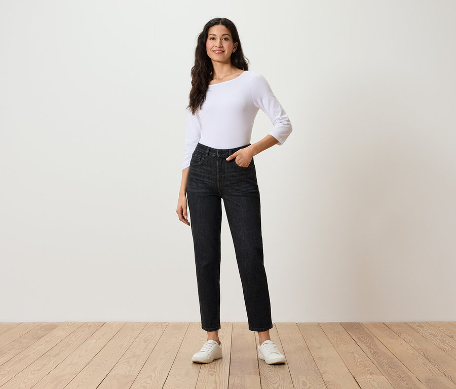 Frau posiert in schwarzen Jeans, weißem Dreiviertelarm-Top und weißen Turnschuhen.