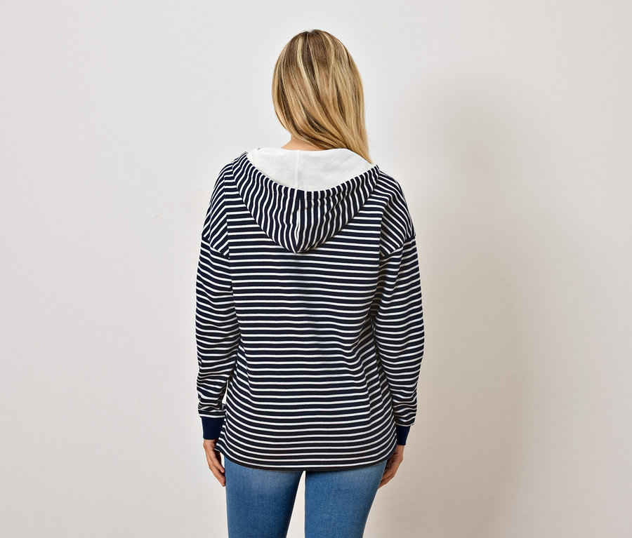 Von hinten ist eine Frau mit blonden Haaren zu sehen, die einen blau-weiß gestreiften Kapuzenpullover und Jeans trägt.