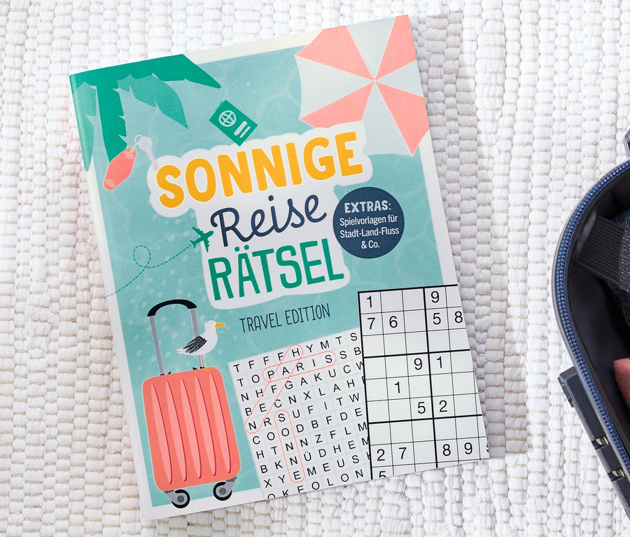 Buch »Sonnige Reise Rätsel« liegt neben einem offenen Koffer.
