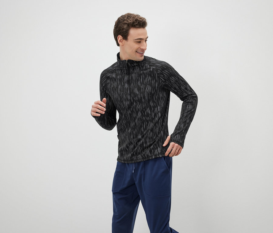 Mann in einem schwarzen, langärmeligen Sportoberteil und blauen Trainingshosen.