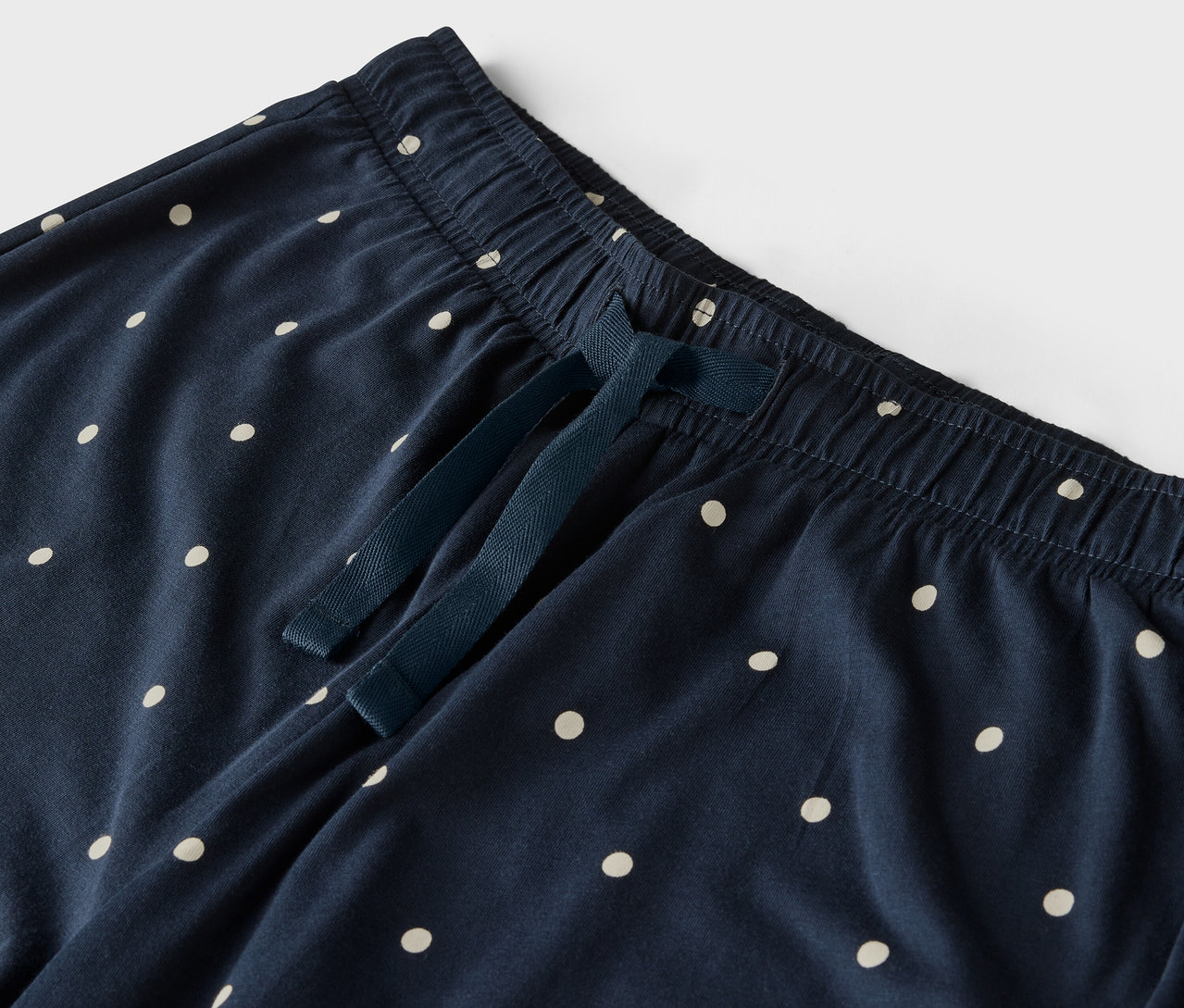 Detail einer blauen Hose mit weißen Tupfen, elastischem Bund und Kordelzug.