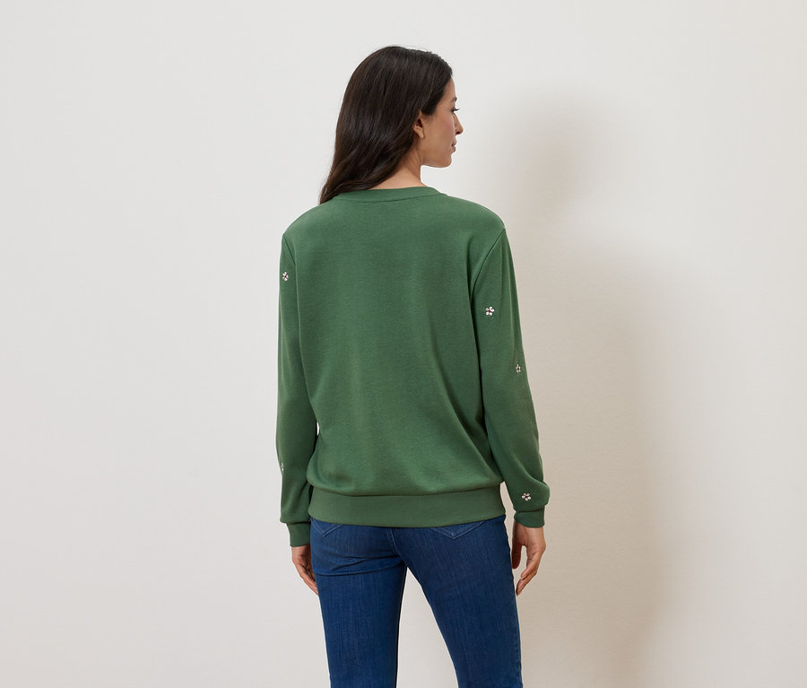 Rückansicht einer Frau mit langen dunklen Haaren, die einen grünen Pullover und Jeans trägt.