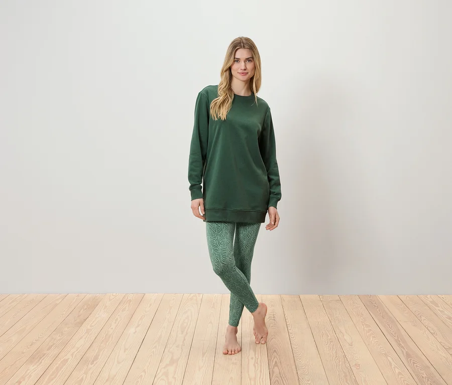 Frau steht und trägt eine grüne Tunika und grüne Leggings.