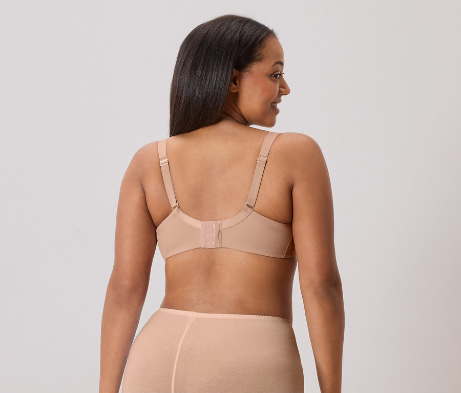 Rückansicht einer Frau mit langen, dunklen Haaren, die einen hautfarbenen BH und passende Unterwäsche trägt.