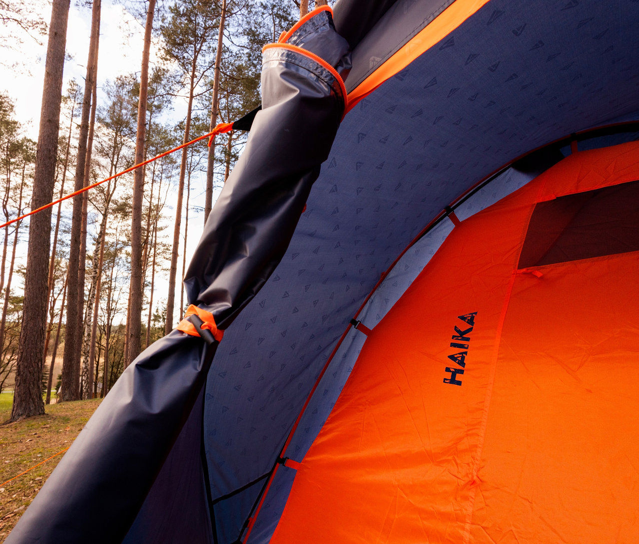 Innenansicht eines Tambu »HAIKA 2« 2-Personen-Kuppelzelts mit orangefarbenem Außenzelt und blauem Innenzelt vor Bäumen.