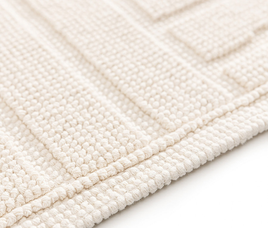 Nahaufnahme einer cremefarbenen Badematte mit erhabenem geometrischen Muster.