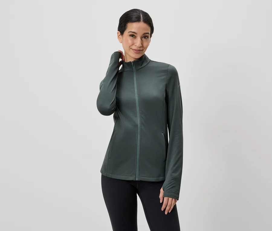 Frau mit hochgesteckten Haaren, die eine grüne Jacke mit Reißverschluss und schwarze Leggings trägt.