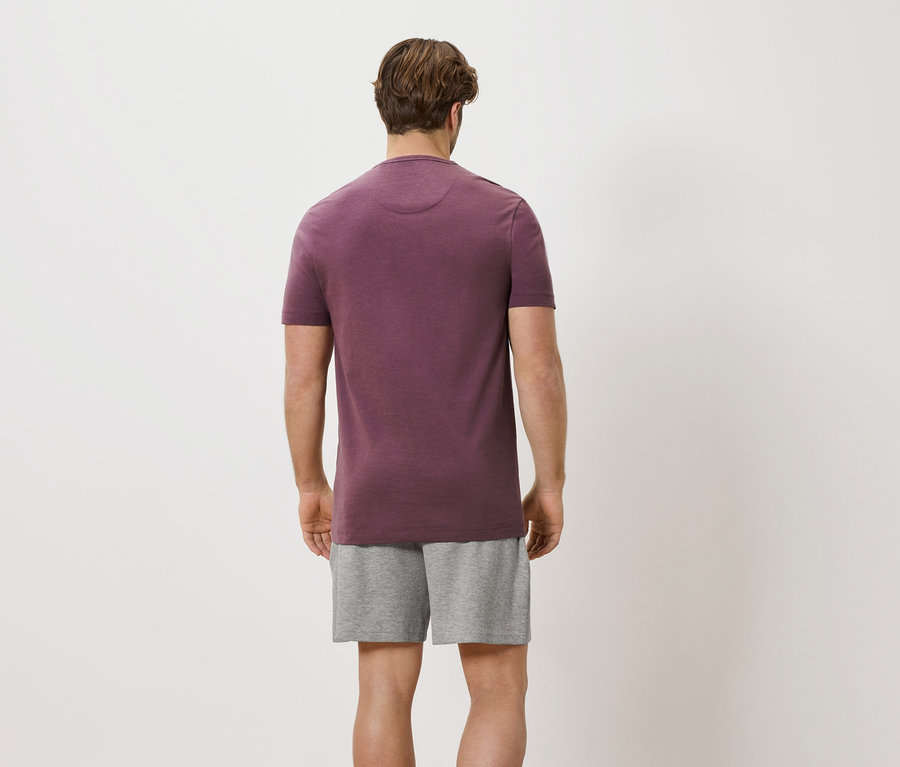 Mann von hinten in weinrotem T-Shirt und grauen Shorts vor weißem Hintergrund.
