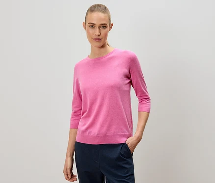 Frau mit einem rosa Pullover und einer marineblauen Hose.