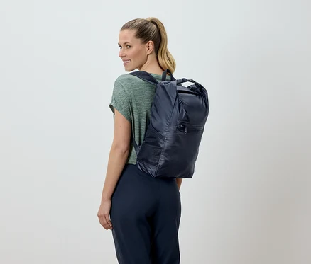 Frau mit blonden Haaren, von hinten gesehen, trägt einen marineblauen Rucksack.