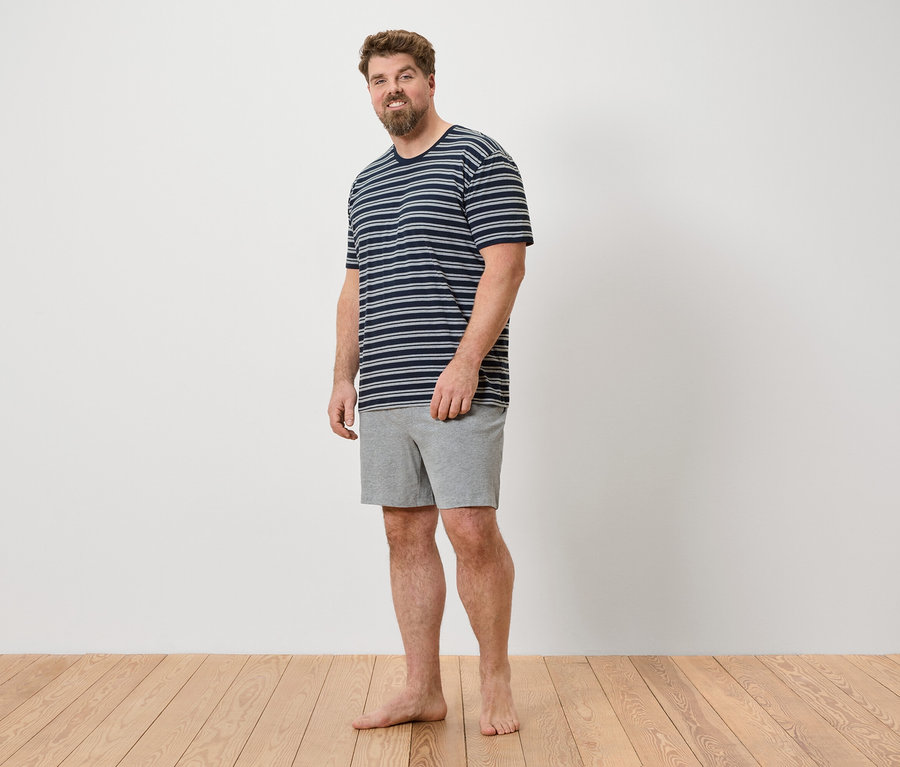Ein Mann steht barfuß auf einem Holzboden und trägt ein gestreiftes T-Shirt und graue Shorts.