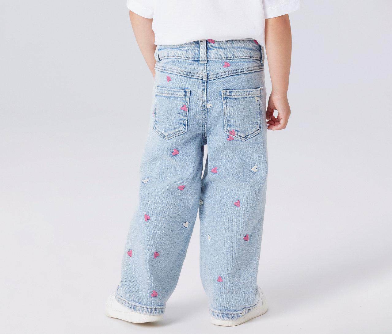 Kind von hinten in NAME IT Kinder-Wide Leg Jeans mit Herzchenmuster und weißen Schuhen.