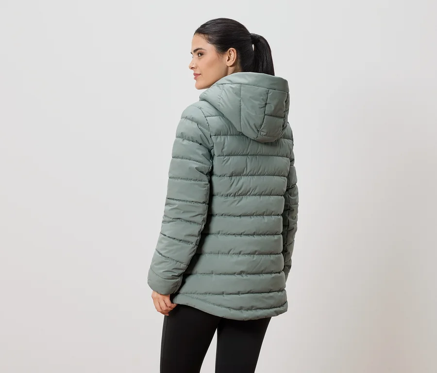 Eine Frau mit Pferdeschwanz trägt eine hellgrüne, gesteppte Jacke mit Kapuze und schwarze Leggings, von hinten gesehen.