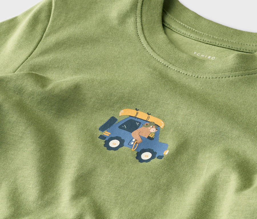 Grünes T-Shirt mit einem Bären, der in einem blauen Auto mit Gepäck auf dem Dach fährt.