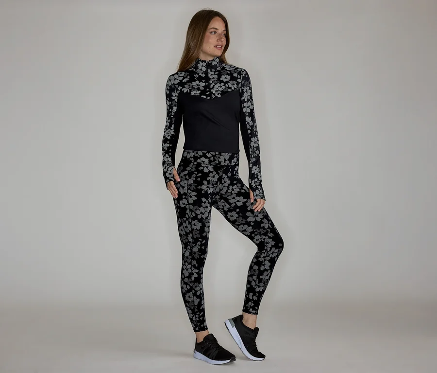 Frau in floral gemustertem, langärmligem Oberteil und Leggings, dazu schwarze Turnschuhe.