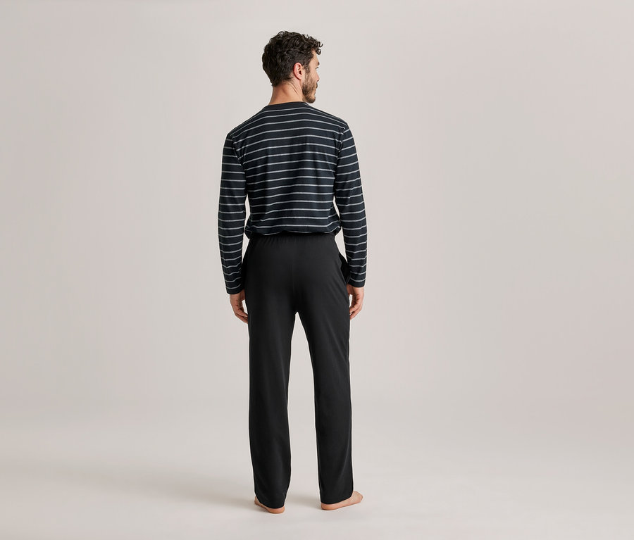 Mann von hinten in einem schwarz-weiß gestreiften Langarmshirt und schwarzer Hose, blickt nach rechts.