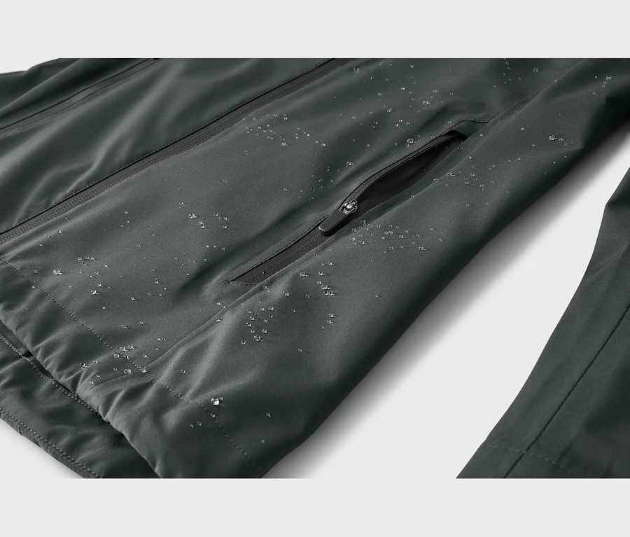 Nahaufnahme einer dunkelgrauen, wasserabweisenden Jacke mit Reißverschluss und Wassertropfen auf dem Stoff.