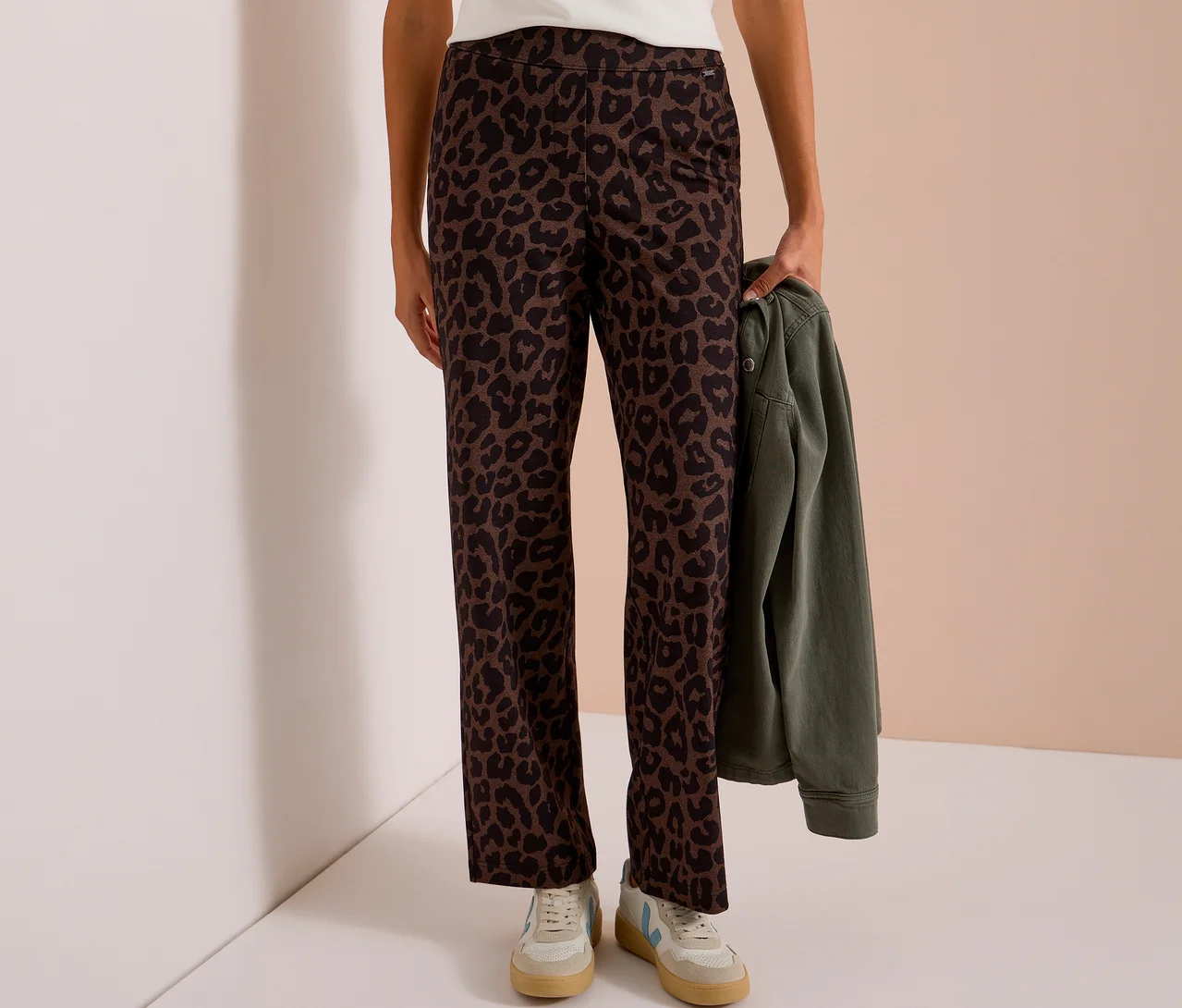 Person trägt eine CECIL Stoffhose mit Alloverprint in Leopardenmuster und hält eine grüne Jacke.