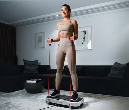 Frau trainiert mit Christopeit Vibrationstrainer Vibro VBT 4200 und roten Widerstandsbändern.