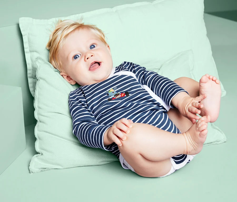 Lächelndes Baby liegt auf dem Rücken und trägt einen blau-gestreiften 3 Langarm-Body.