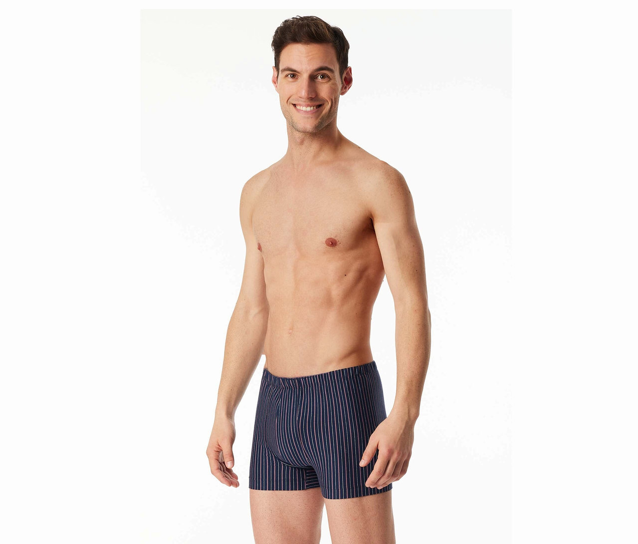 Lächelnder Mann mit freiem Oberkörper trägt gestreifte Boxershorts vor einem weißen Hintergrund.
