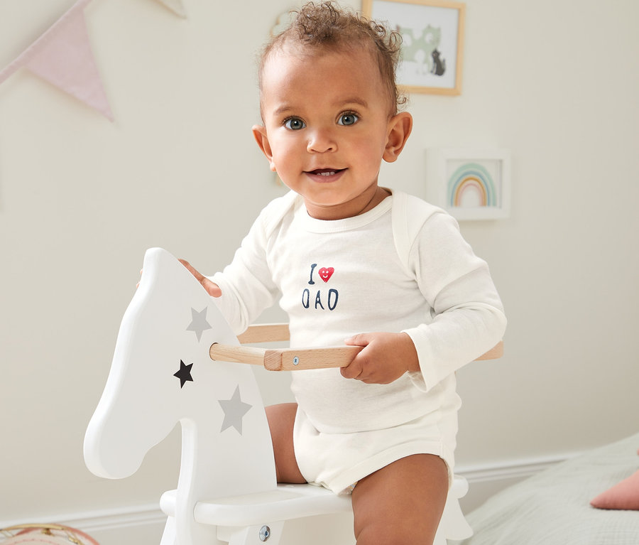 Baby in einem weißen 5er Langarm-Body aus Bio-Baumwolle auf einem Schaukelpferd.