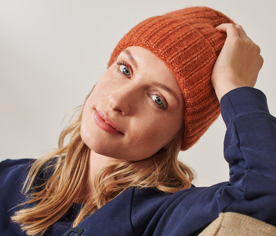 Frau sitzt mit einer orangen Strickmütze mit Wolle.