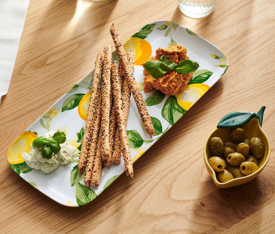 Servierschale mit Brotstangen, zwei Dips und eine Schale Oliven auf einem Holztisch.