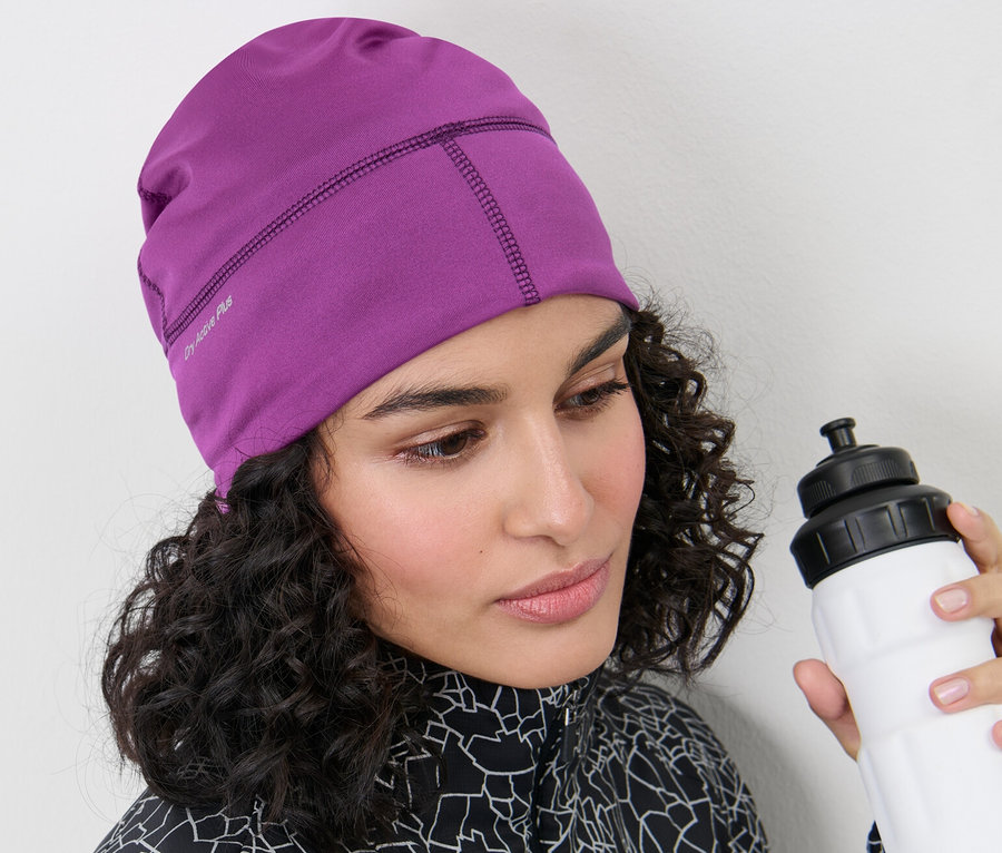Frau mit beerefarbener Thermo-Funktionsmütze und weisser Wasserflasche.