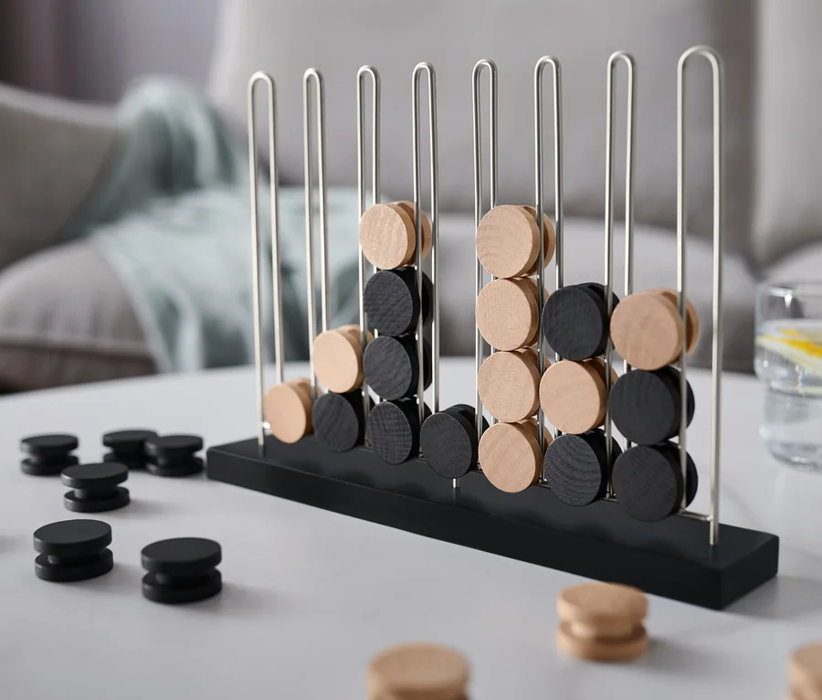 Ein schwarz-beiges Spiel »4 in einer Reihe« steht auf einem Tisch.