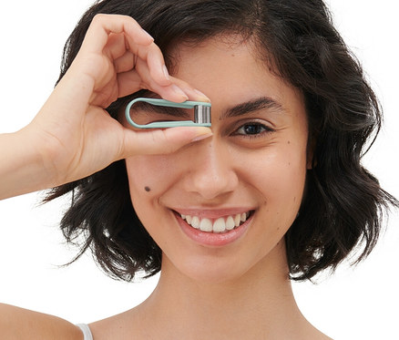 Frau hält einen manuellen Mini-Gesichtshaarentferner vor ihr Auge.